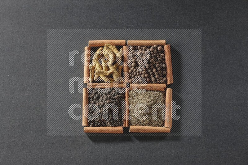 4 مربعات من عيدان القرفة ممتلئة بحبوب الفلفل الأسود والكمون وبهار الفلفل الحلو وأصابع الكركم على أرضية سوداء