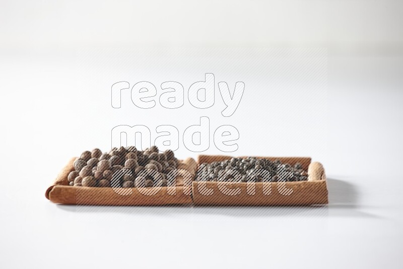 2 squares of cinnamon sticks full of black peppers and allspice on white flooring