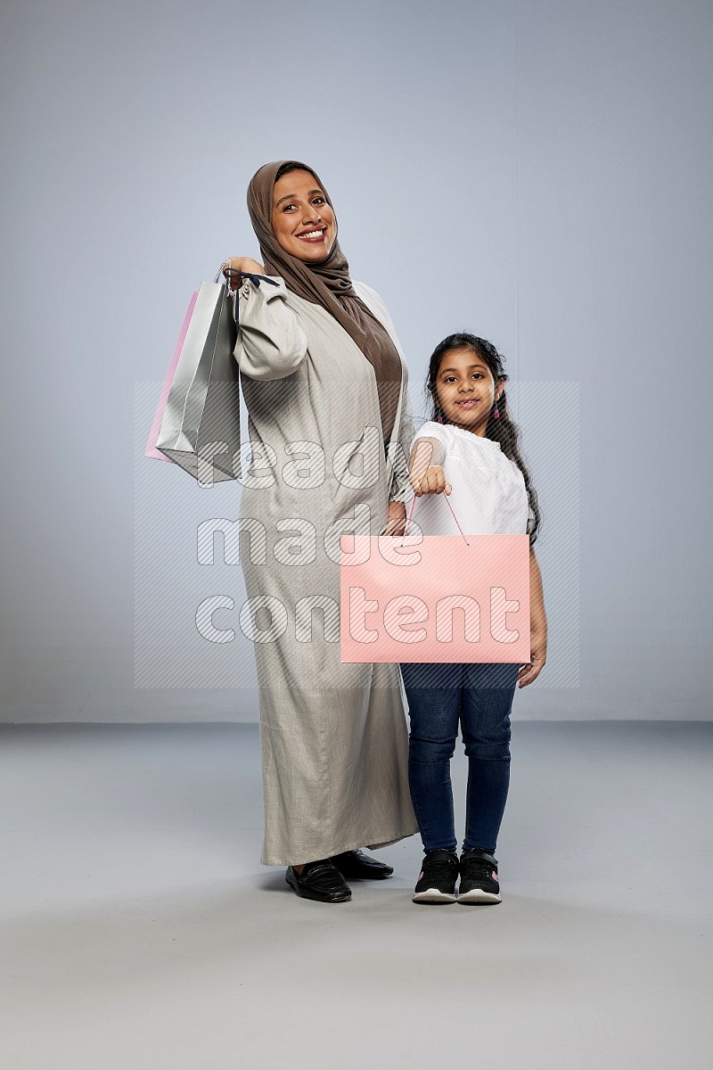 Mom and daughter holding shopping bags on gray background