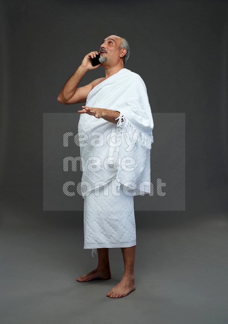 A man wearing Ehram Standing talking on phone on gray background