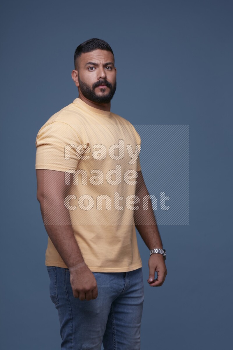A man posing in a blue background wearing a yellow shirt