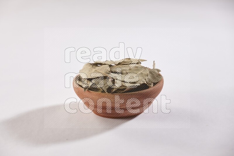 A wooden bowl filled with dried bay leaves on white flooring in different angles