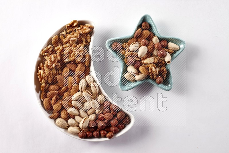 Mixed nuts in a crescent pottery plate and a star shaped plate on white background