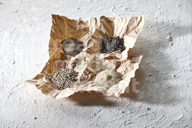 Crumpled pieces of paper full of black and white pepper beads and powder on a textured white flooring