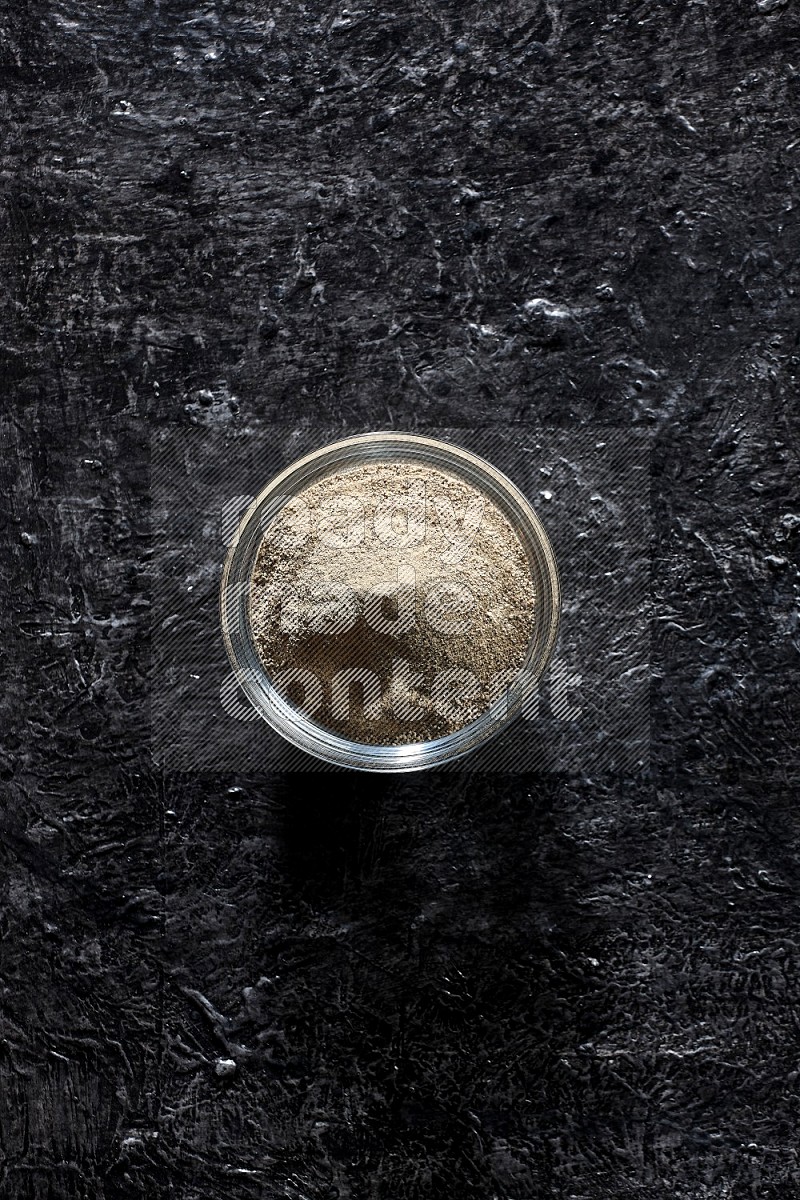 A glass bowl full of white pepper powder on textured black flooring