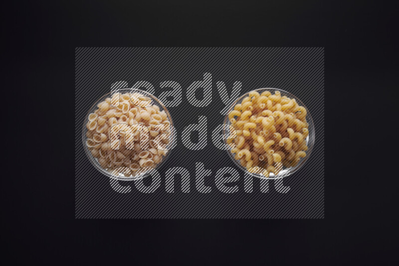 Different pasta types in glass bowls on black background