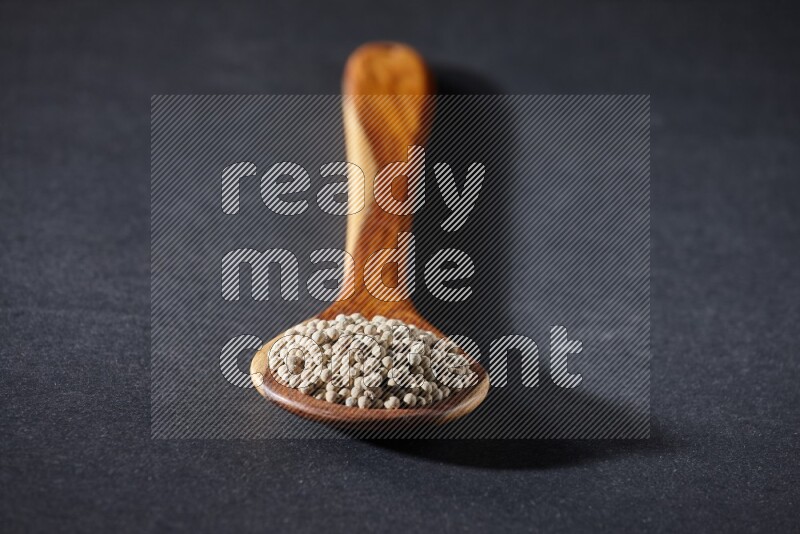 A wooden ladle full of white pepper beads on black flooring