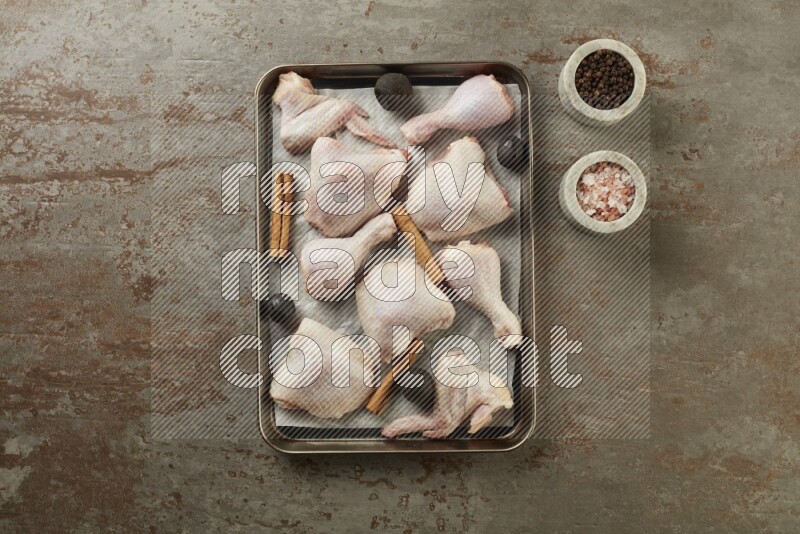 Mixed fresh chicken pieces in an oven tray on a textured rustic background