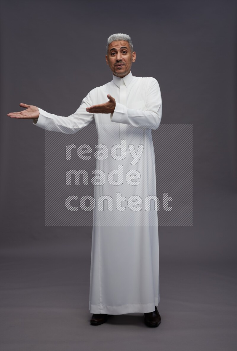 Saudi man wearing thob standing interacting with the camera on gray background