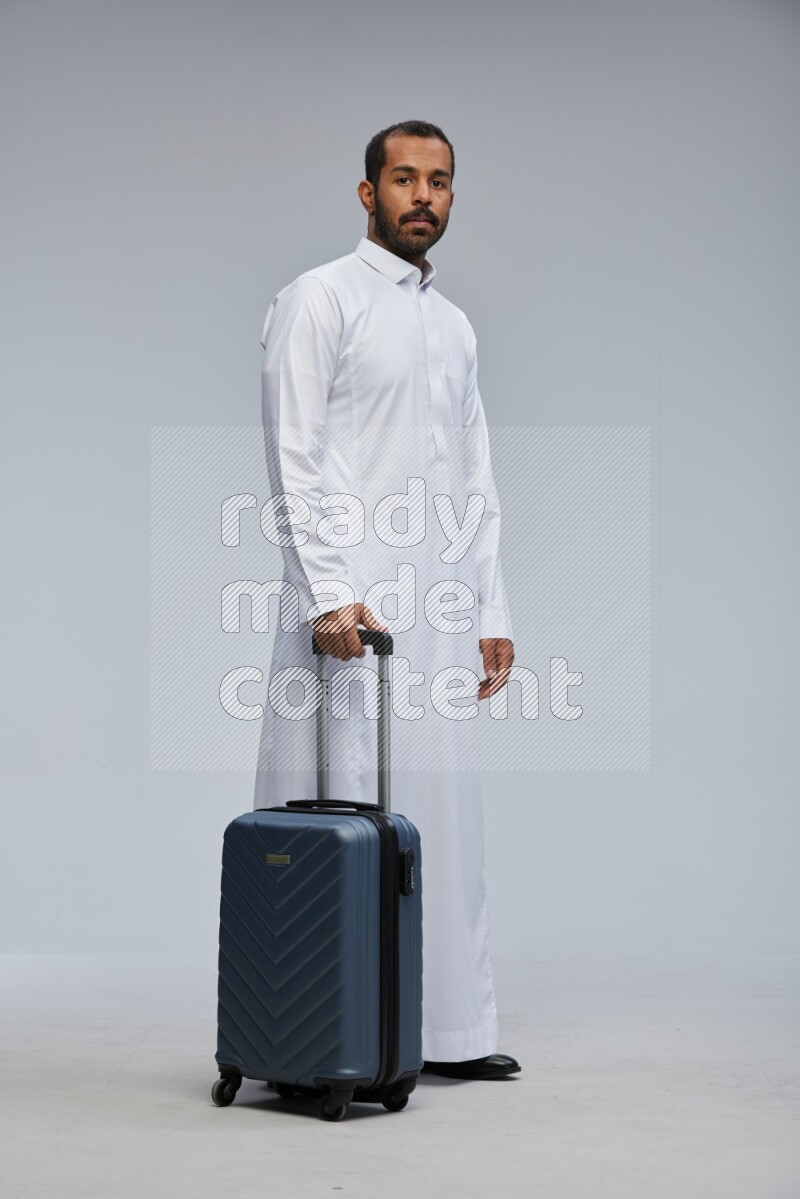 Saudi man wearing thob standing holding Travel bag on Gray background