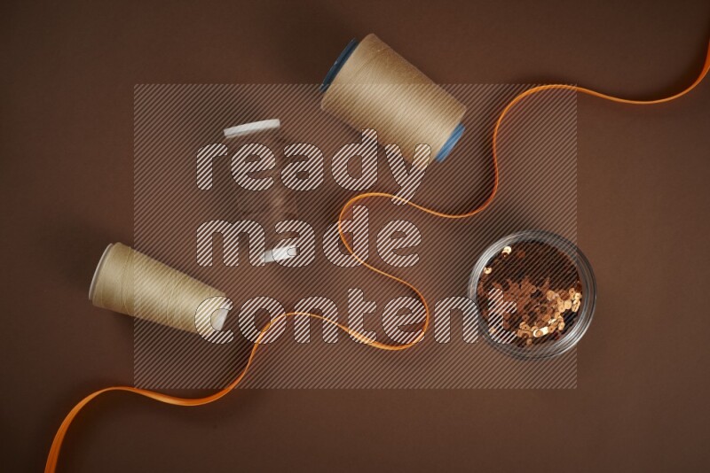An orange collection of sewing and tailoring tools arranged on a brown background