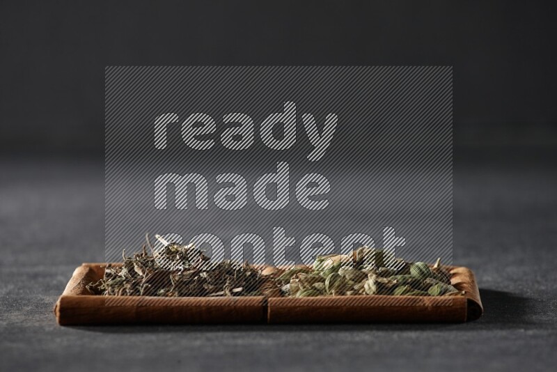 2 squares of cinnamon sticks full of cardamom and dried basil on black flooring