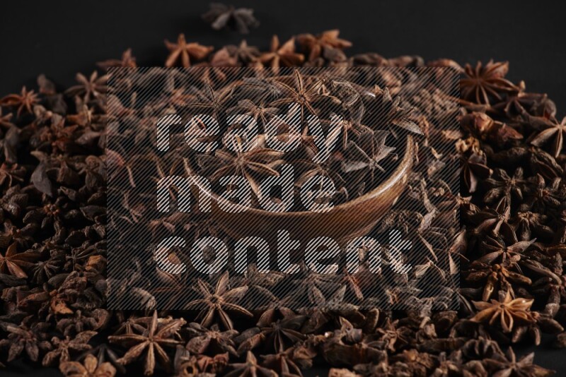 Star Anise in a wooden bowl and surrounded by more anise filling the frame on black flooring