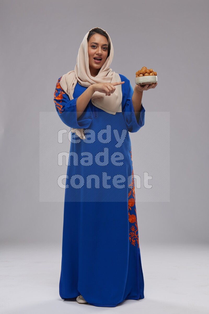 A Saudi woman standing wearing Jalabeya holding a plate of luqaimat