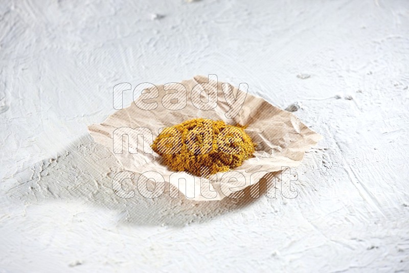 Turmeric powder in a crumpled piece of paper on textured white flooring