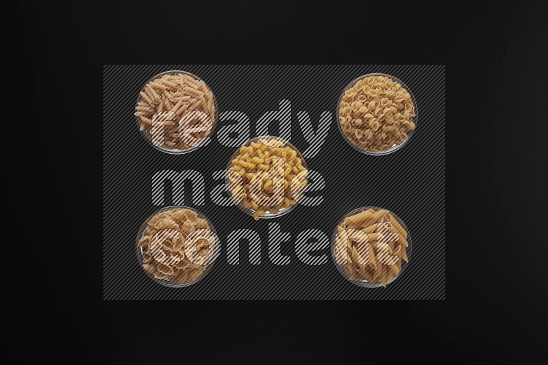 Different pasta types in 5 glass bowls on black background