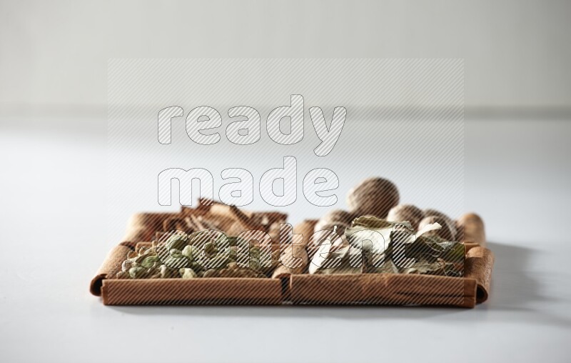 4 مربعات من أعواد القرفة ممتلئة بجوزة الطيب وأوراق الغار وحبوب الهيل والقرفة على أرضية بيضاء