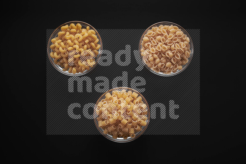 Different pasta types in glass bowls on black background