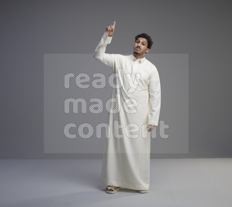 A Saudi man standing wearing thob interacting with the camera on gray background