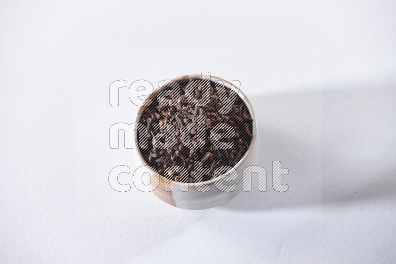A beige ceramic bowl full of cloves on a white flooring