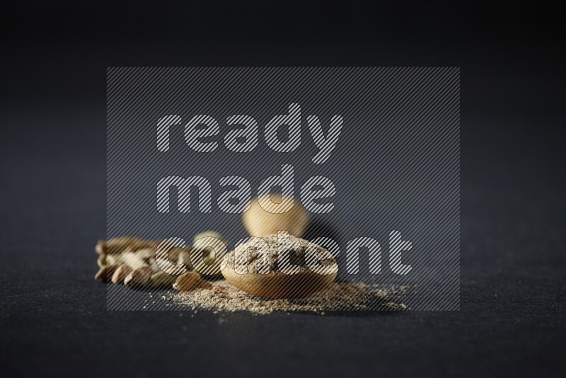 ملعقة خشبية ممتلئة ببودرة الهيل وحبوب الهيل بجانبها على خلفية سوداء