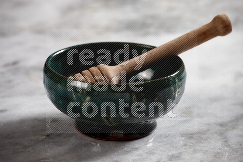 Dark green Pottery Bowl with wooden honey handle in it, on grey marble flooring, 15 degree angle