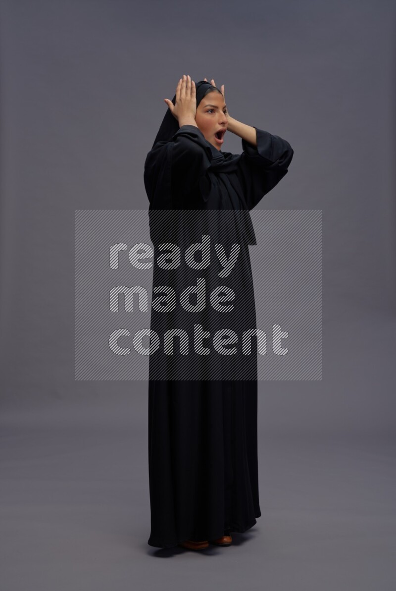 Saudi woman wearing Abaya standing hands behind head on gray background