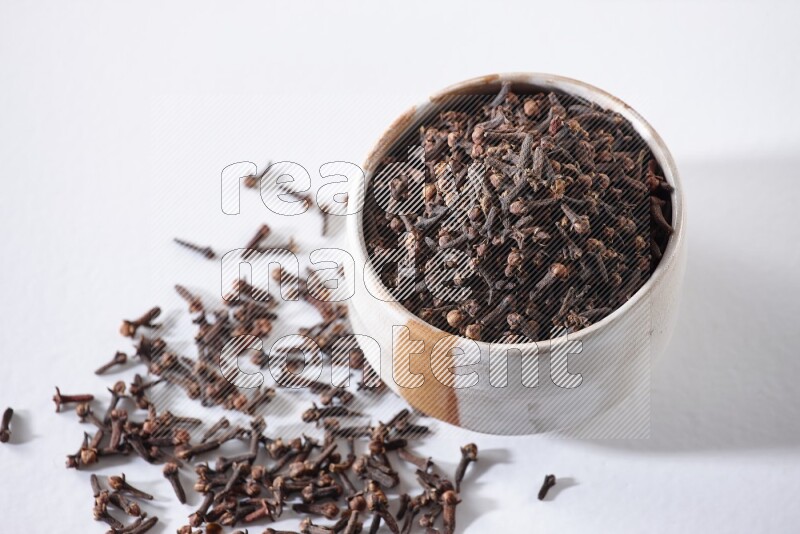 A beige ceramic bowl full of cloves on a white flooring
