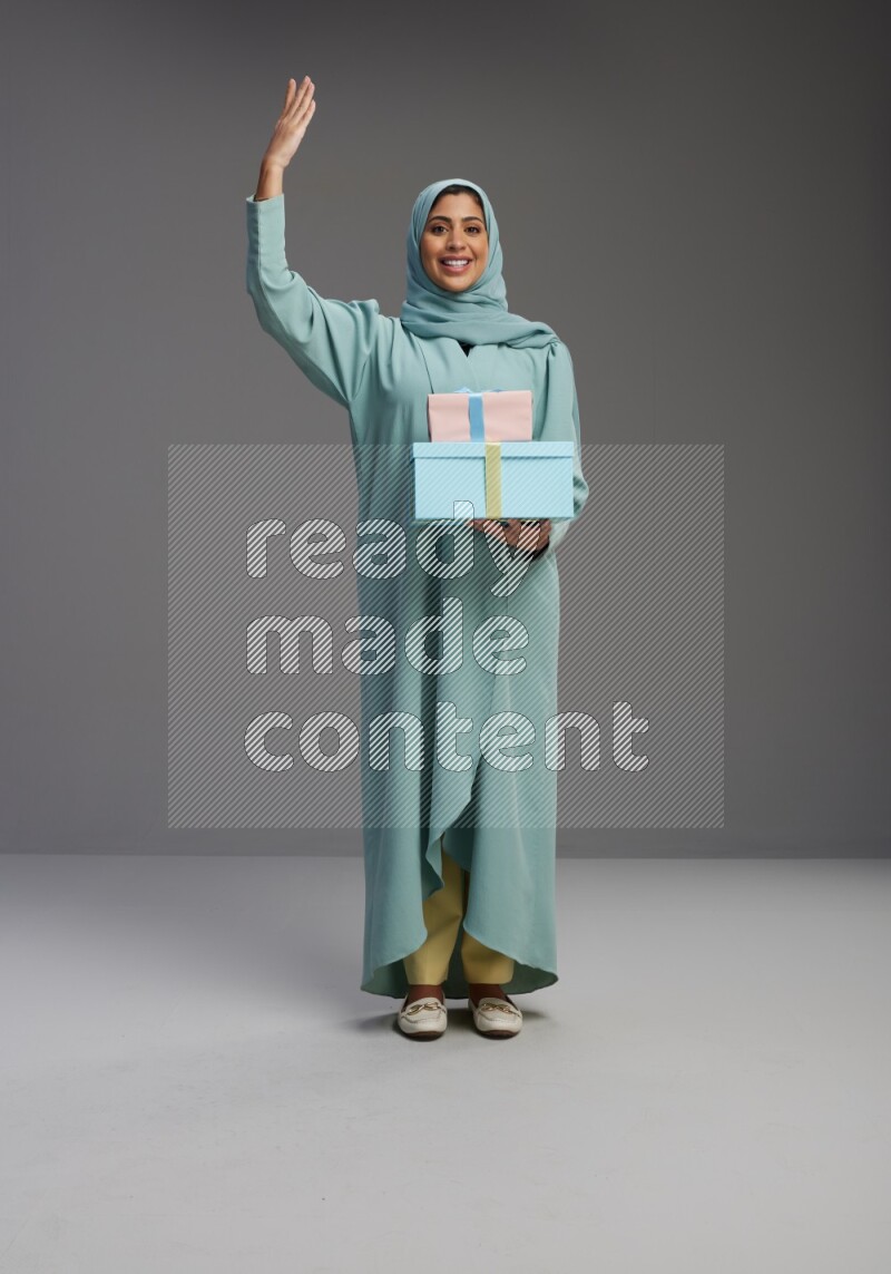 Saudi Woman wearing Abaya standing holding gift box on Gray background