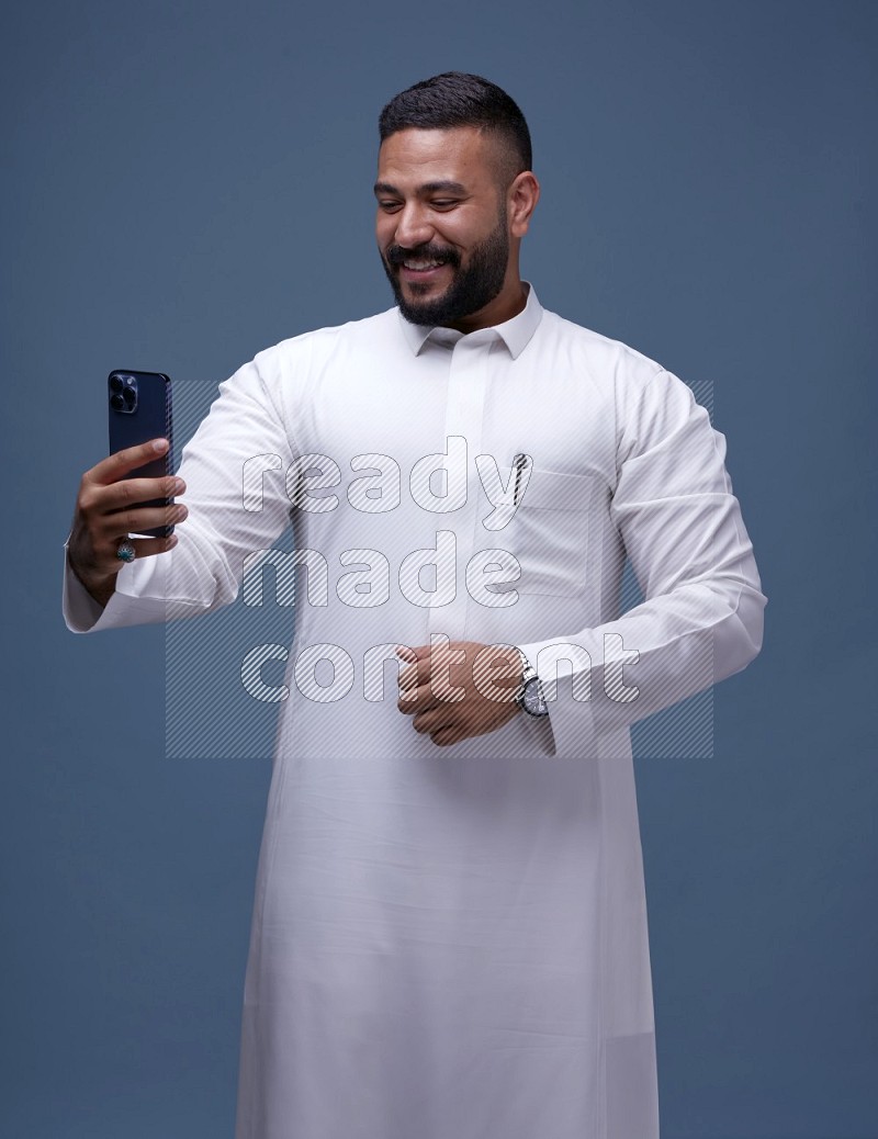 رجل سعودي يرتدي ثوب ابيض ويتصور بجواله