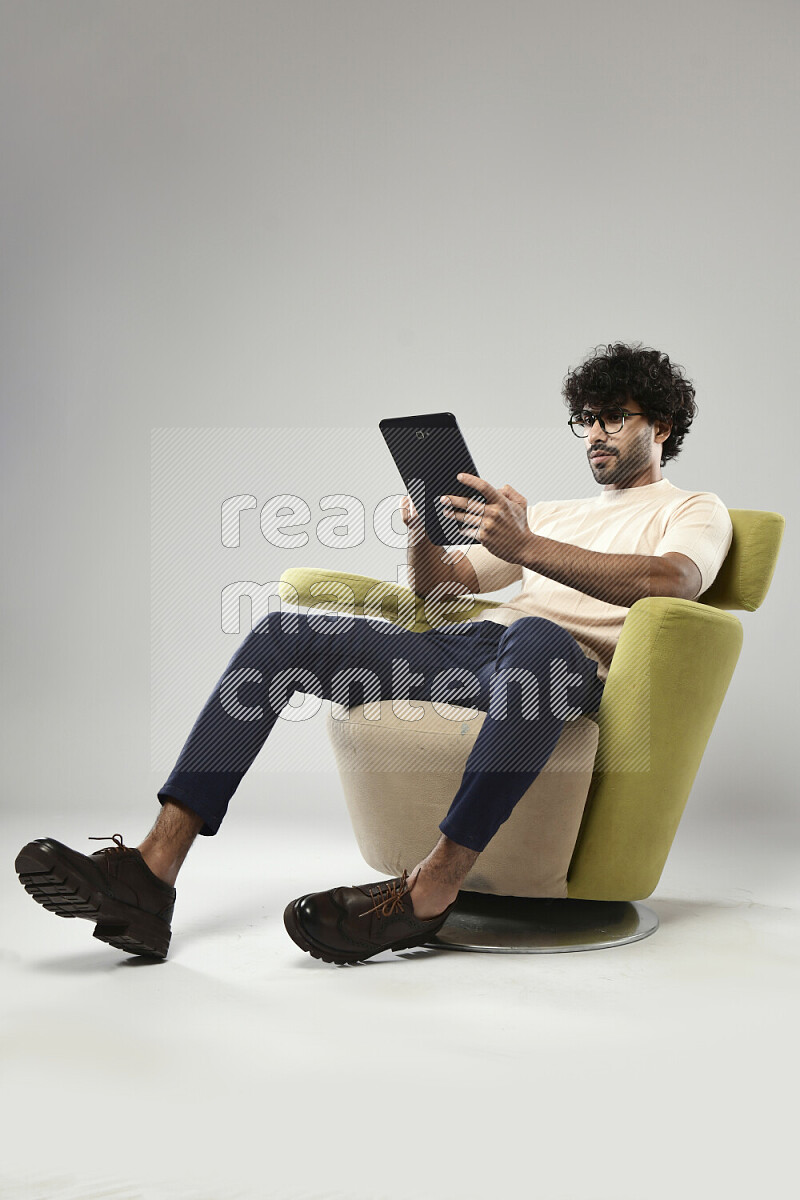 A man wearing casual sitting on a chair browsing on a tablet on white background