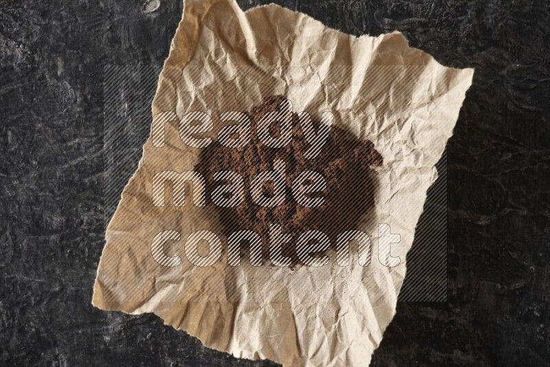 Cloves powder in crumpled piece of paper on a textured black flooring