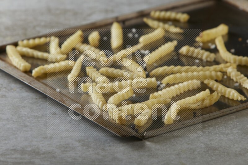 crinkle fries in a black stainless steel rectangle tray on grey textured counter top
