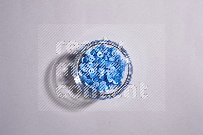 A glass bowl full of colored buttons on grey background