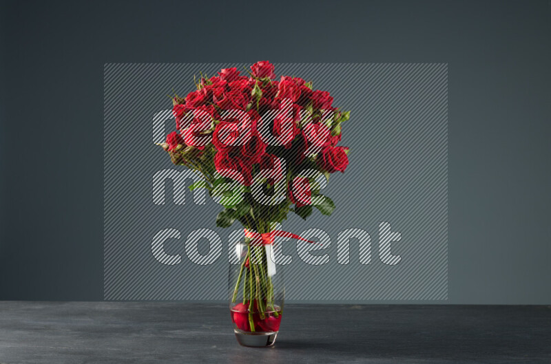 An arrangement of vivid red roses tightly bound with a red ribbon in a glass vase on black marble background