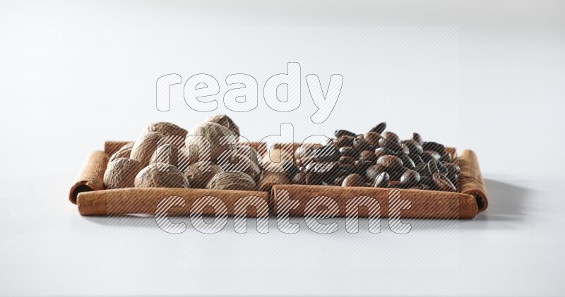 مربعان من أعواد القرفة ممتلئان بحبوب القهوة وجوزة الطيب علي خلفية بيضاء