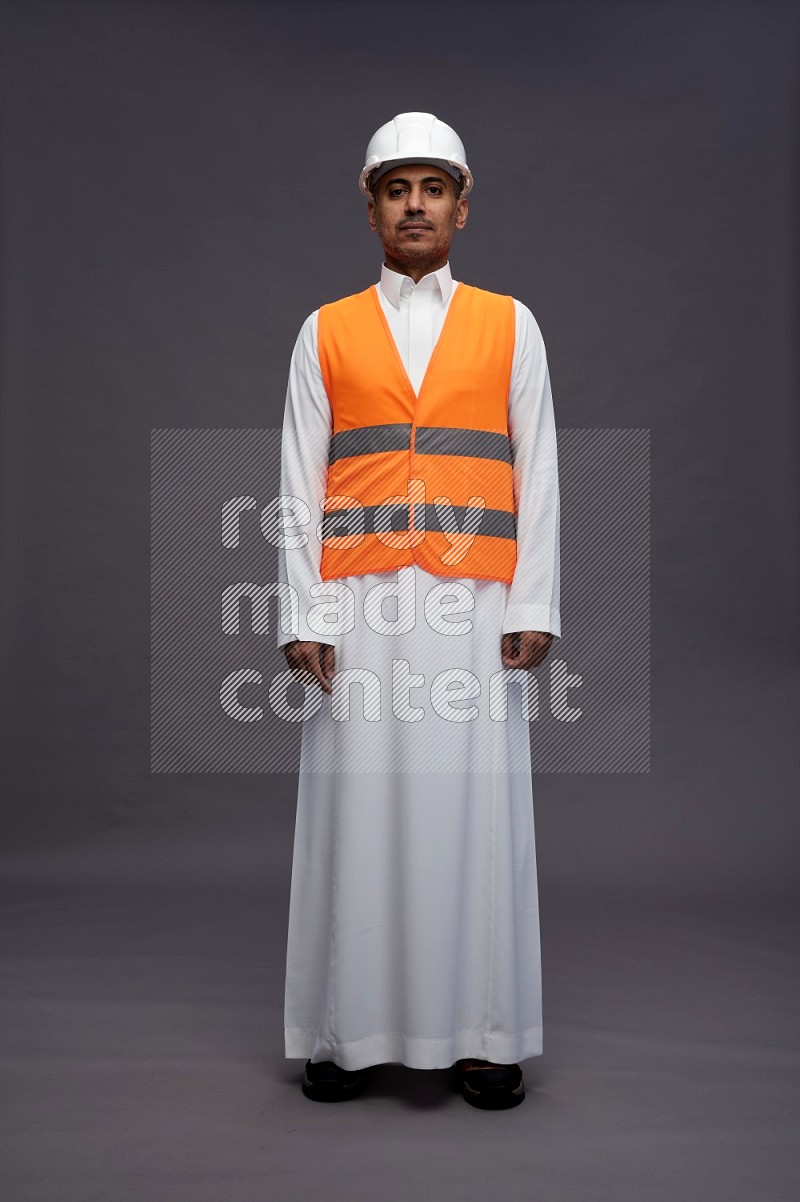 Saudi man wearing thob with engineer vest standing interacting with the camera on gray background