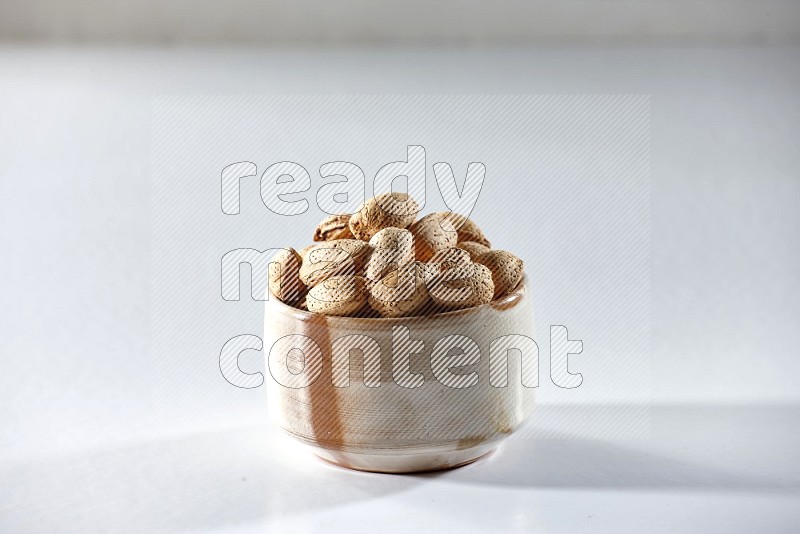 A beige ceramic bowl full of almonds on a white background in different angles