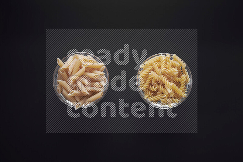 Different pasta types in glass bowls on black background