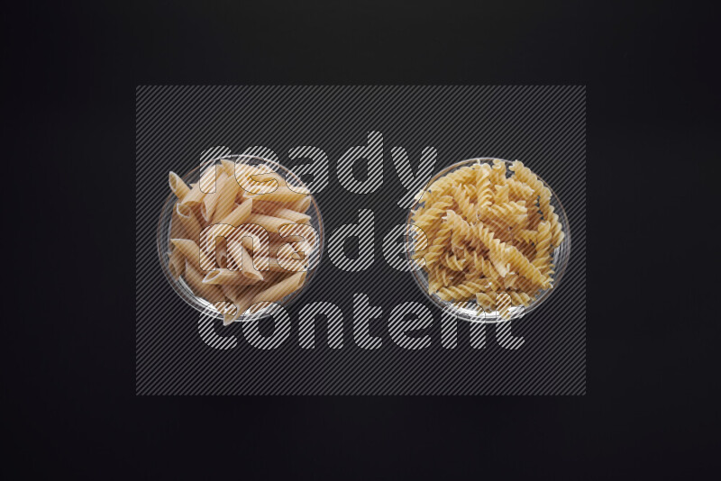 Different pasta types in glass bowls on black background