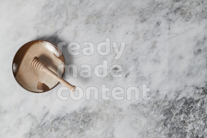 Multicolored pottery plate with wooden honey dipper in it on grey marble background