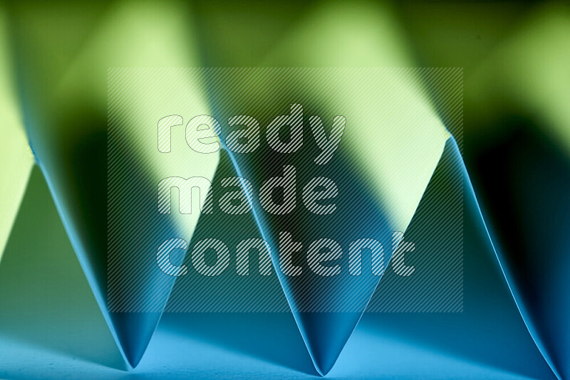 A close-up abstract image showing sharp geometric paper folds in green and blue gradients
