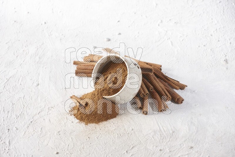 Ceramic beige bowl over filled with cinnamon powder and cinnamon sticks around the bowl on a textured white background in different angles