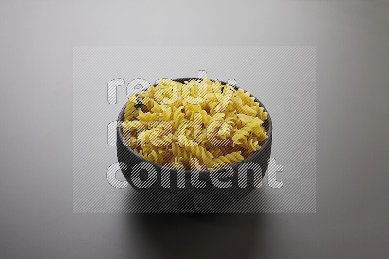 Fusilli pasta in a pottery bowl on grey background
