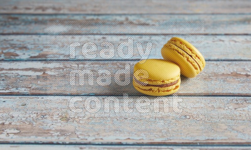 45º Shot of two Yellow Lemon macarons on light blue wooden background