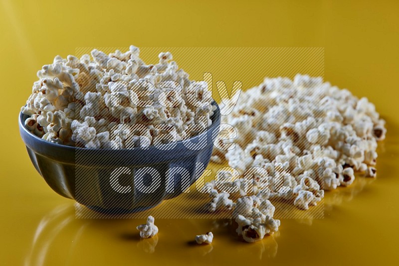 A blue pottery bowl full of popcorn with popcorn beside it on a yellow background in different angles
