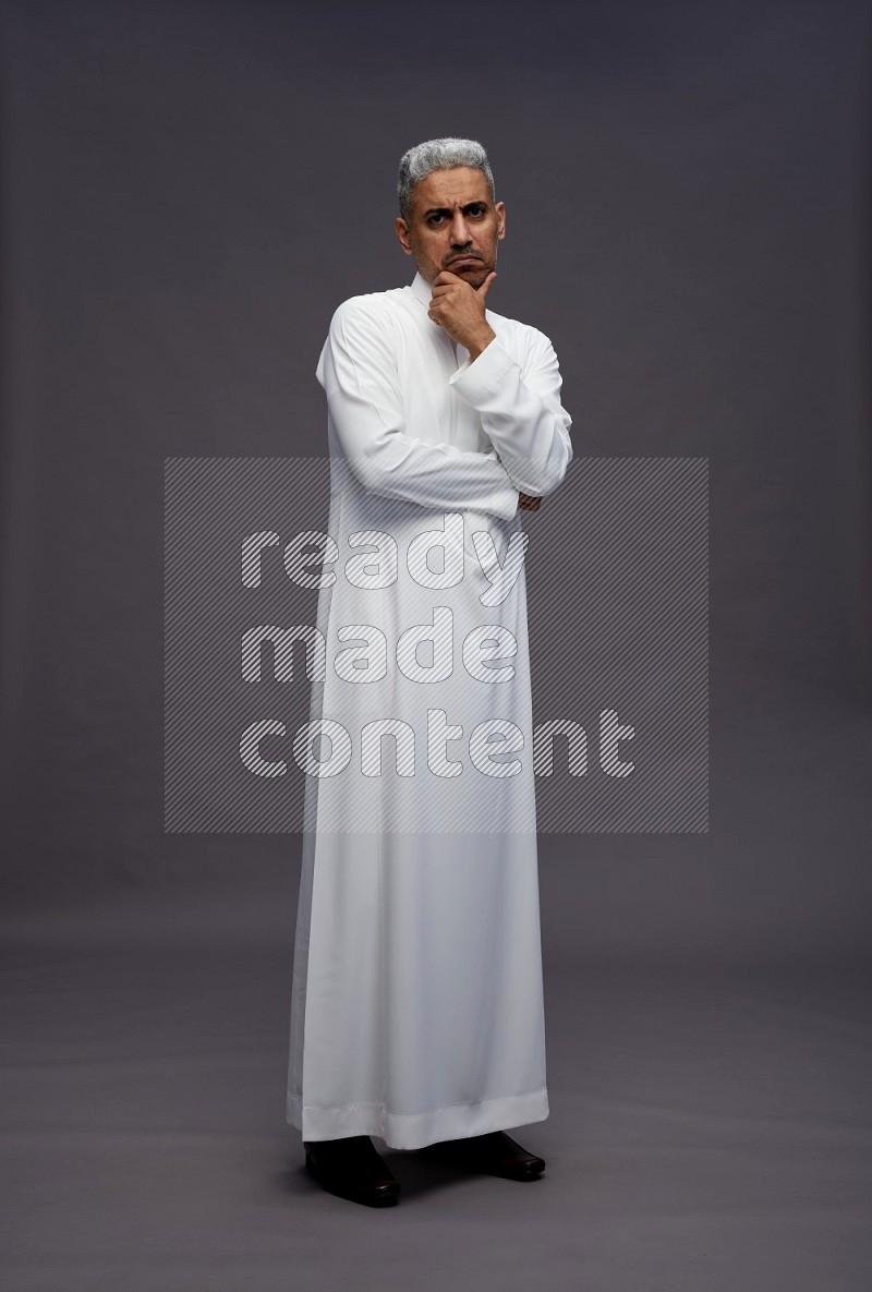 Saudi man wearing thob standing interacting with the camera on gray background