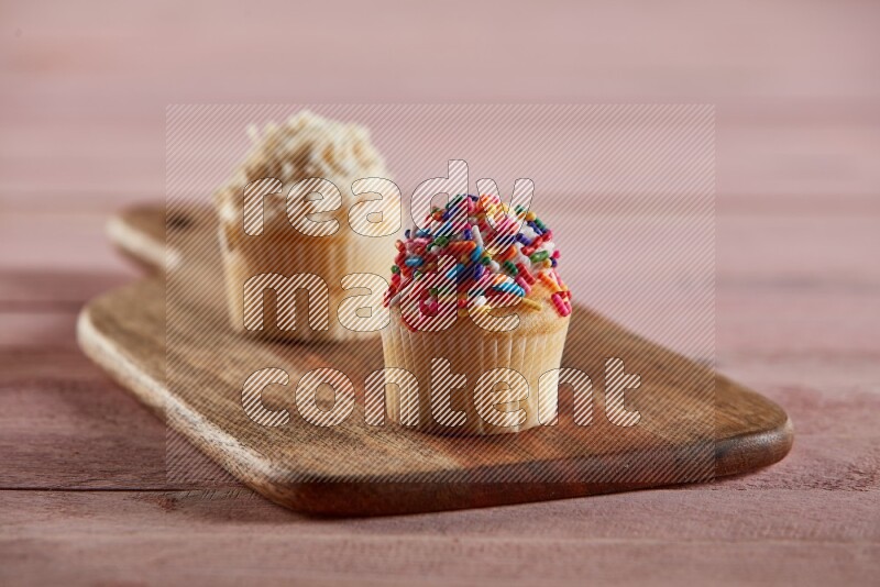 Vanilla mini cupcake topped with sprinkles on a wooden board