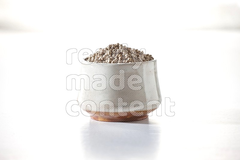 وعاء فخار بيج ممتلئ بحبوب الفلفل الأبيض على أرضية بيضاء