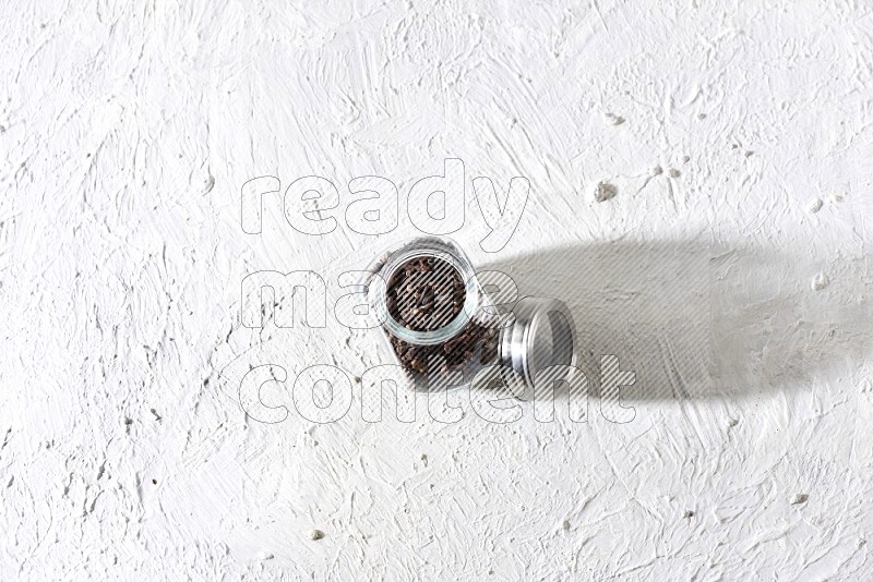 وعاء زجاجي للبهارات ممتلئ بحبوب القرنفل على أرضية بيضاء
